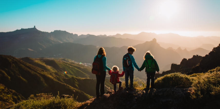 Familienurlaub: Mutter mit drei Kindern beim Wandern hält einen Moment still und bewundert das wunderschöne grüne Bergpanorama.