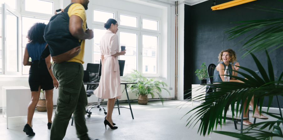 Sinnbild für Desksharing: ein modernes helles Büro, eine Angestellte ist bereits am Schreibtisch, drei weitere Kollegen kommen dazu