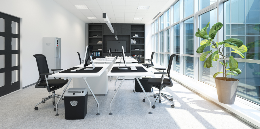 Desksharing schafft Struktur: ein modernes, helles und aufgeräumtes Büro mit eines langen Fensterfront rechts, sechs Tischen und Bürostühle. An der hinteren Wand ein Einbauschrank mit einigen Ordnern und einem großen Bildschirm für digitale Meetings.