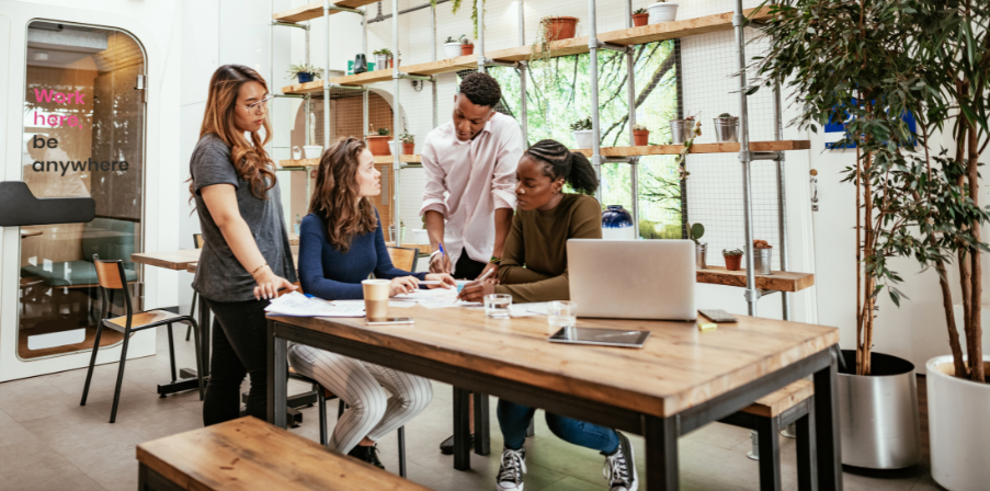 Vier Menschen arbeiten zusammen an einem Besprechungstisch in einem flexiblen Büro.