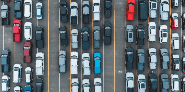 Luftaufnahme eines Parkplatzes mit vielen geparkten Fahrzeugen in verschiedenen Farben und Reihen.