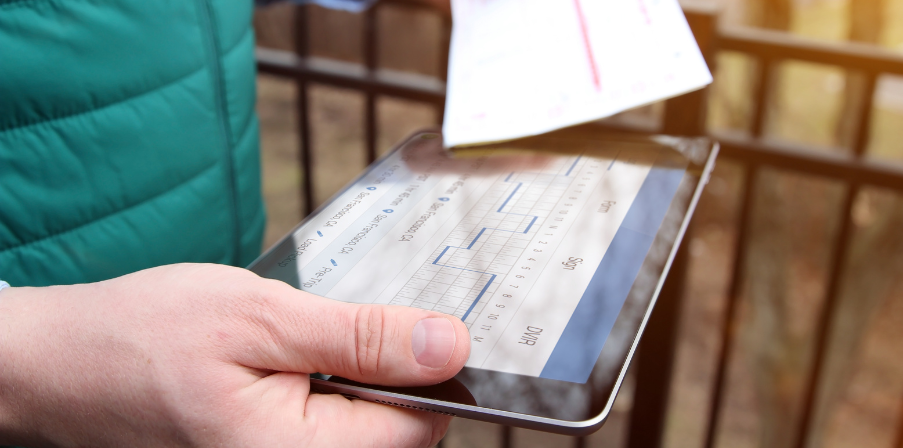 Eine Nahaufnahme eines Tablets in der einen Hand und eines Zettels in der anderen Hand - abgleichend. 